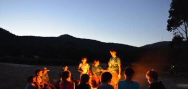 group of children sitting around a camp fire in early evening