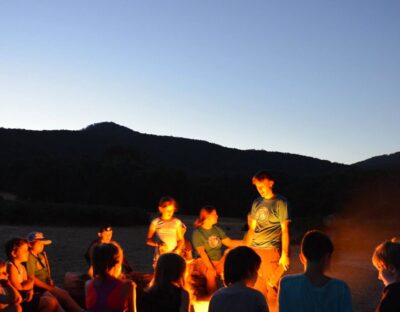 group of children sitting around a camp fire in early evening