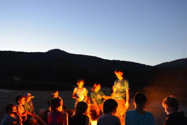 group of children sitting around a camp fire in early evening