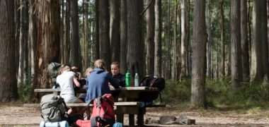 Group of children sitting at a campsite table with hiking bags and water bottles