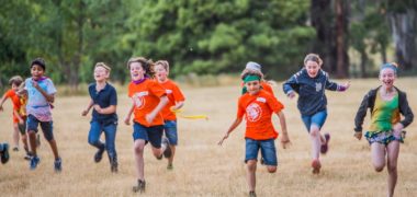 Group of kids running and smiling across a grass field at Cave Hill Creek