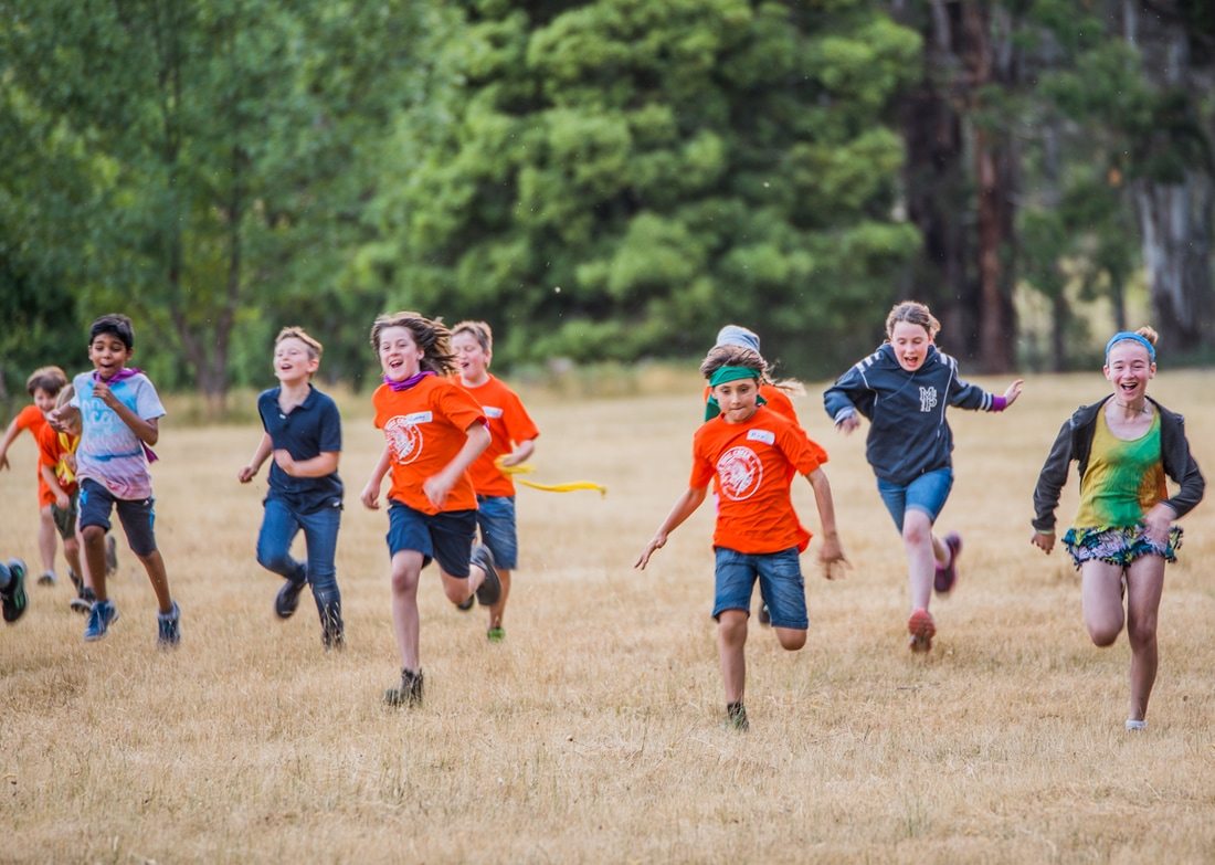 Group of kids running and smiling across a grass field at Cave Hill Creek