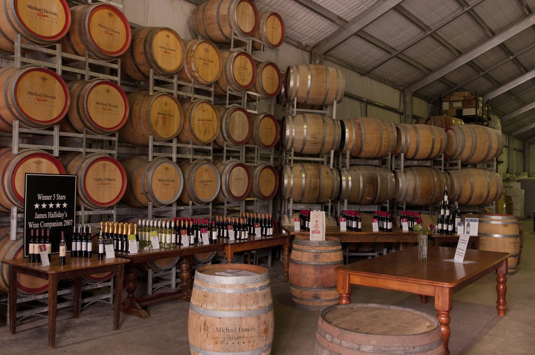 Stacked Michael Unwin wine barrels with bottles of unopened wines showcased on tables.