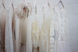 Close up images of white and light pink occasion dresses on clothing rack with white brick background