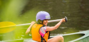 Image of smiling girl paddling a canoe in Cave Hill Creek