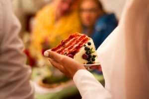Close up image of bride holding a slice of layered cake with frosting and berries on top