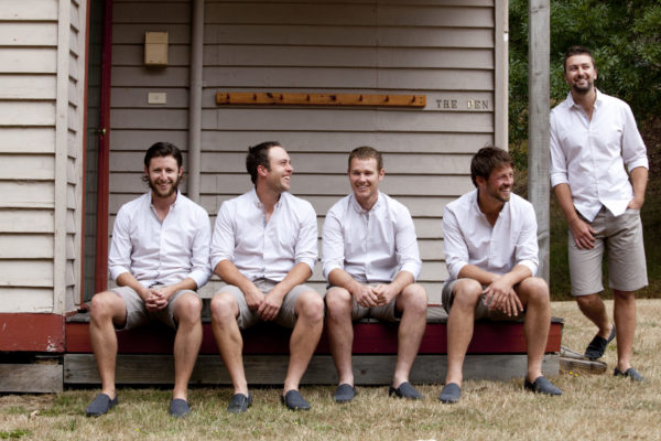 Wedding image of groomsmen wearing matching outfits seated outside The Den building