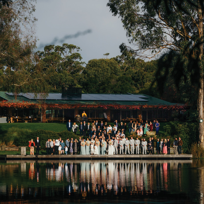 Evening view of the lodge across the lake with wedding guests gathered for a group photograph