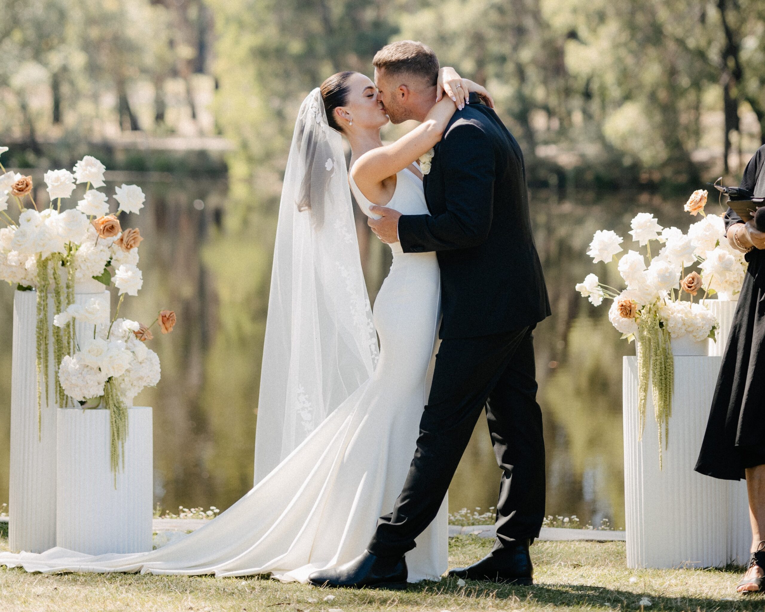 Bride and groom kissing by the lake at Cave Hill Creek with floral pillars
